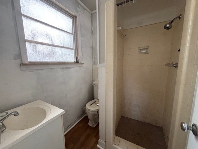 bathroom featuring hardwood / wood-style flooring, a healthy amount of sunlight, a tile shower, and toilet