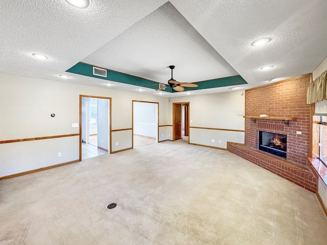 unfurnished living room featuring light carpet, a textured ceiling, a fireplace, and a tray ceiling