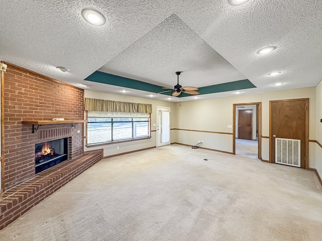 unfurnished living room with carpet floors, a brick fireplace, a textured ceiling, and a tray ceiling