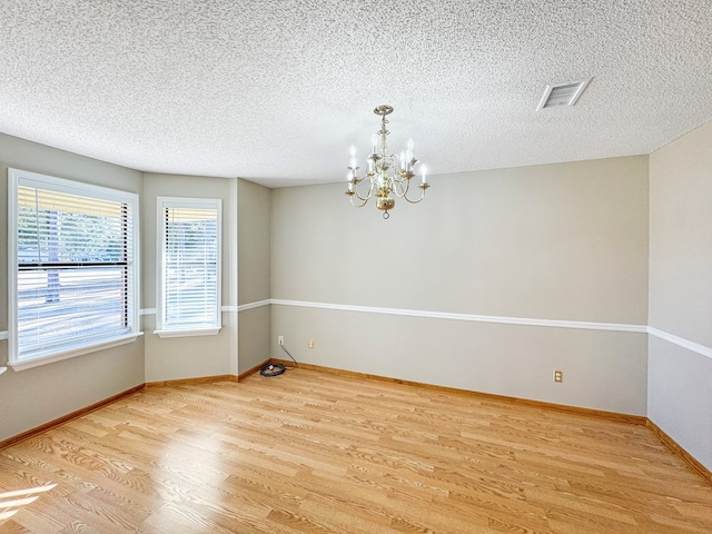 empty room featuring a textured ceiling, light wood-type flooring, and a chandelier