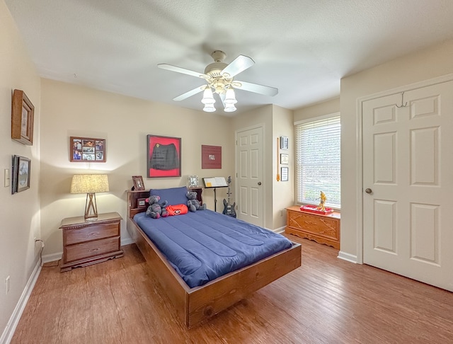 bedroom with light wood-style floors, ceiling fan, baseboards, and a textured ceiling