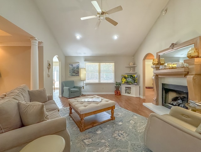 living area featuring light wood-style floors, arched walkways, a fireplace with raised hearth, and high vaulted ceiling