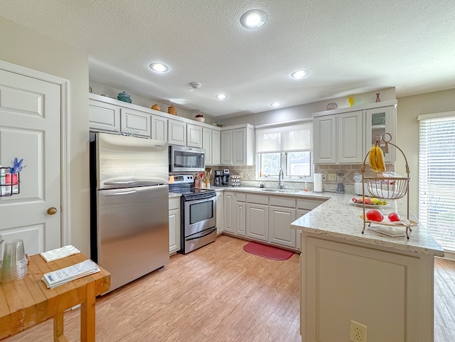 kitchen with tasteful backsplash, appliances with stainless steel finishes, a sink, light wood-type flooring, and a peninsula