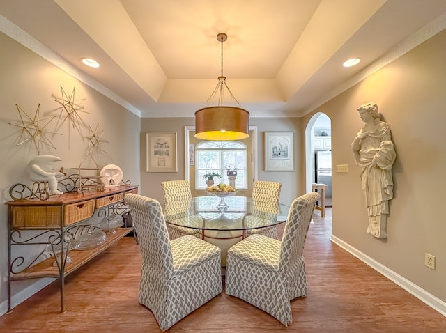 dining space featuring arched walkways, recessed lighting, wood finished floors, baseboards, and a raised ceiling