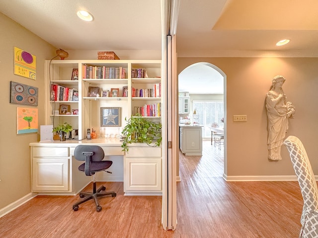 home office with light wood-style flooring, arched walkways, baseboards, and built in study area