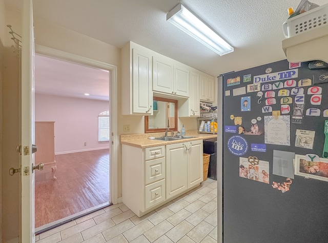 kitchen featuring a textured ceiling, a sink, white cabinetry, light countertops, and freestanding refrigerator