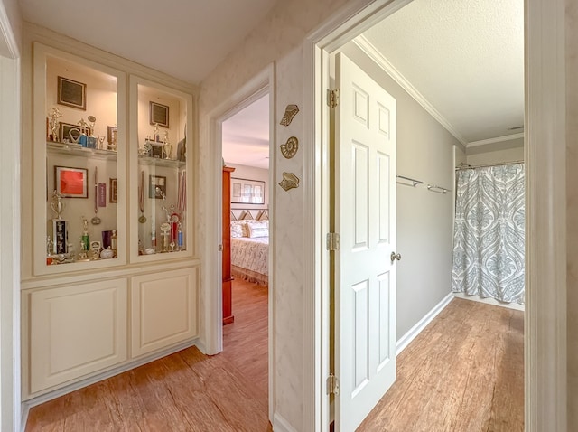 corridor featuring light wood-style floors, crown molding, a textured ceiling, and baseboards