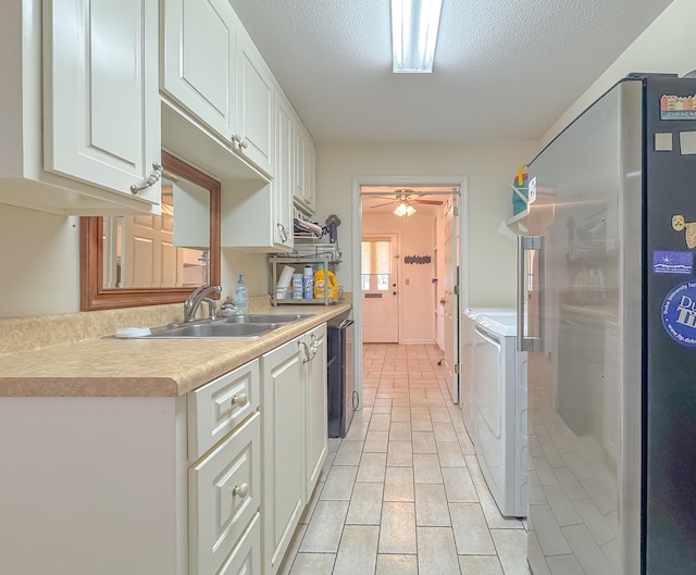 kitchen featuring white cabinets, freestanding refrigerator, light countertops, washing machine and dryer, and a sink