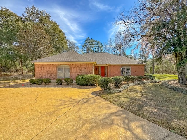 ranch-style house featuring a shingled roof, a front yard, and brick siding