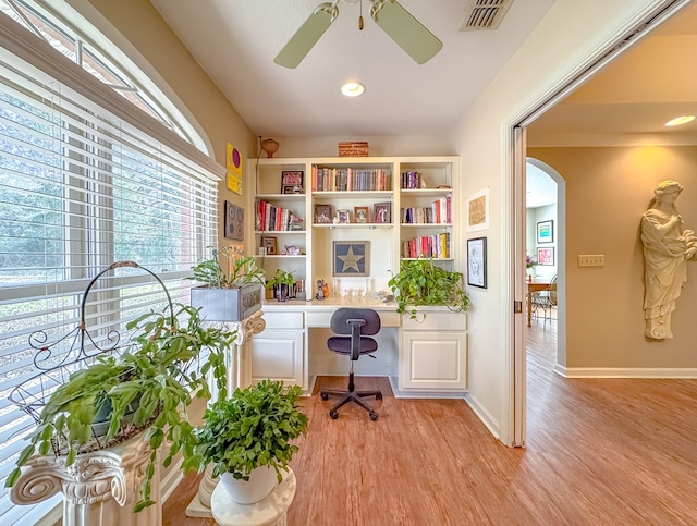 office area with arched walkways, visible vents, light wood-style flooring, built in study area, and ceiling fan