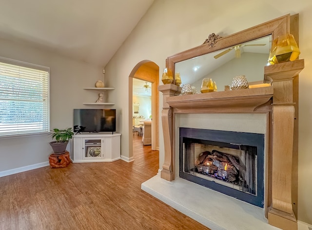 sitting room with arched walkways, a ceiling fan, vaulted ceiling, wood finished floors, and a lit fireplace