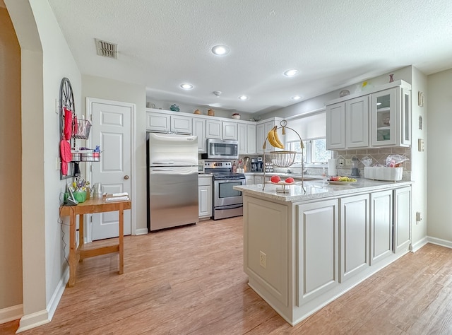 kitchen with light wood finished floors, white cabinets, glass insert cabinets, appliances with stainless steel finishes, and a peninsula