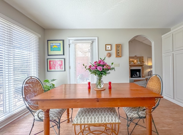 dining room with light wood-style flooring, arched walkways, a fireplace with raised hearth, and a textured ceiling