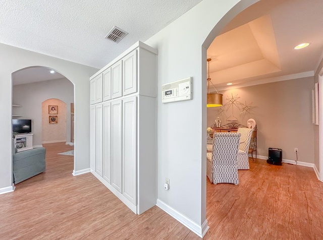 hall with arched walkways, light wood-style flooring, visible vents, and baseboards