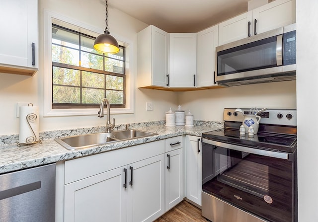 kitchen featuring light stone countertops, white cabinetry, sink, stainless steel appliances, and decorative light fixtures