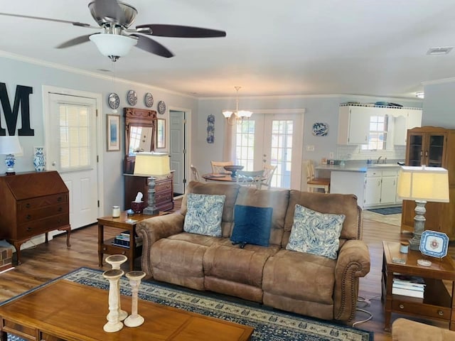 living room featuring french doors, ceiling fan with notable chandelier, ornamental molding, and wood-type flooring