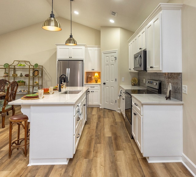 kitchen with stainless steel appliances, pendant lighting, vaulted ceiling, a center island with sink, and white cabinets