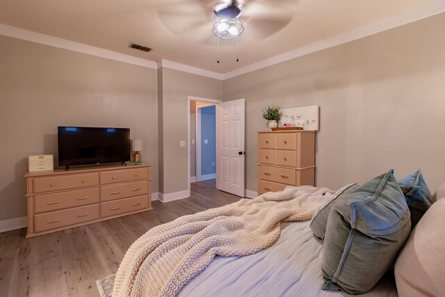 bedroom featuring a ceiling fan, visible vents, wood finished floors, baseboards, and ornamental molding