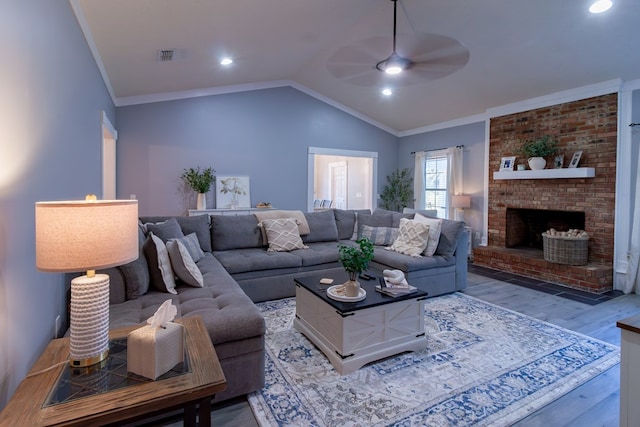 living area with a ceiling fan, wood finished floors, crown molding, lofted ceiling, and a brick fireplace