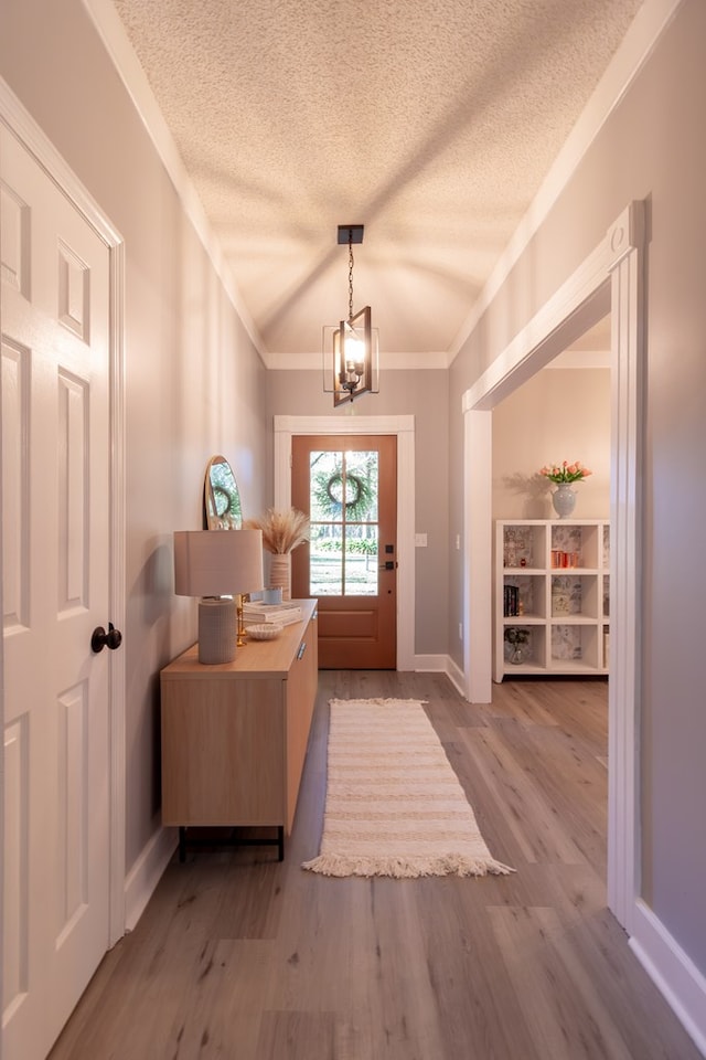 foyer entrance featuring a textured ceiling, wood finished floors, an inviting chandelier, crown molding, and vaulted ceiling