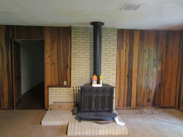 unfurnished living room with a wood stove, wood walls, and light colored carpet