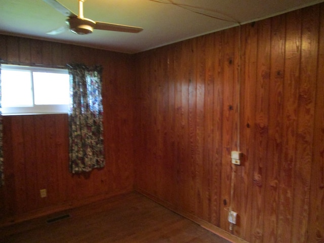 unfurnished room featuring ceiling fan, wood walls, and wood-type flooring