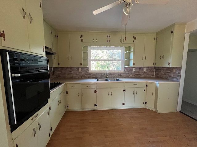 kitchen with sink, black oven, decorative backsplash, and light wood-type flooring