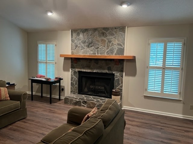 living room with hardwood / wood-style floors, a stone fireplace, and a textured ceiling