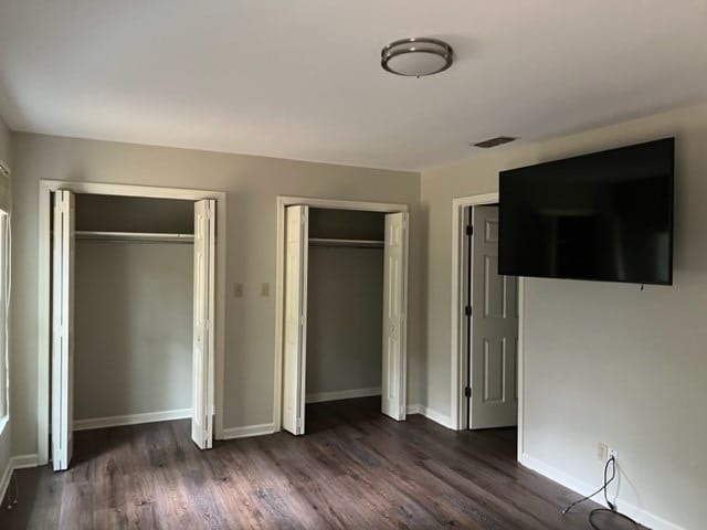 unfurnished bedroom with dark hardwood / wood-style floors and two closets