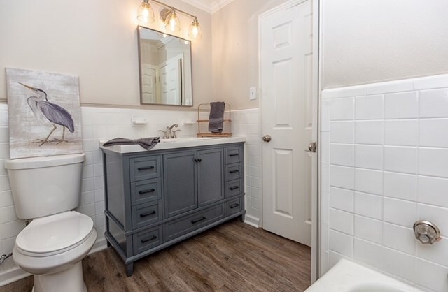 bathroom featuring hardwood / wood-style floors, vanity, ornamental molding, a tub to relax in, and tile walls