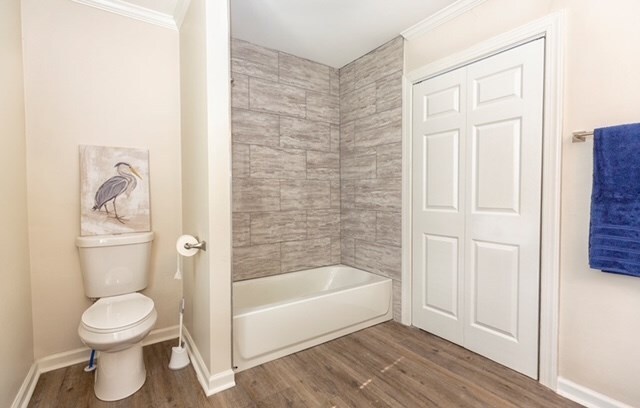 bathroom with hardwood / wood-style floors, washtub / shower combination, toilet, and ornamental molding