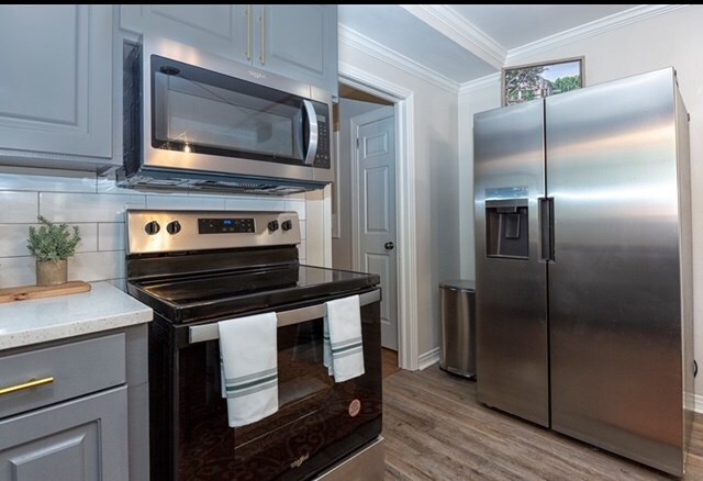 kitchen featuring tasteful backsplash, crown molding, stainless steel appliances, and light wood-type flooring