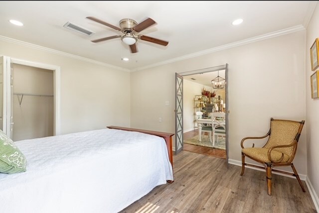 bedroom with hardwood / wood-style flooring, ceiling fan, a spacious closet, ornamental molding, and a closet