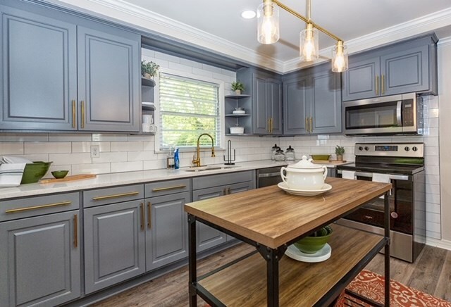 kitchen featuring sink, dark wood-type flooring, backsplash, pendant lighting, and appliances with stainless steel finishes