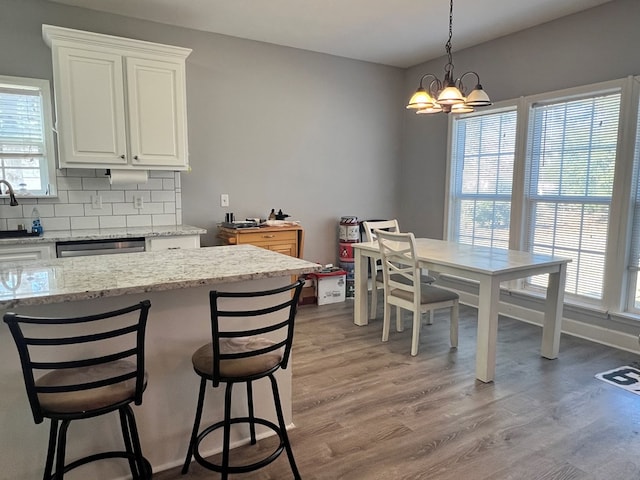 kitchen with light wood-type flooring, tasteful backsplash, light stone counters, white cabinetry, and a chandelier