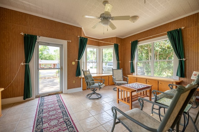 interior space with ornamental molding, ceiling fan, light tile patterned flooring, and wood walls