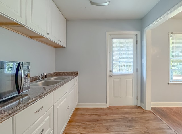 kitchen with sink, dark stone counters, white cabinetry, and light hardwood / wood-style floors