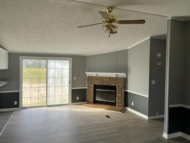 unfurnished living room with a fireplace, a ceiling fan, a textured ceiling, wood finished floors, and baseboards