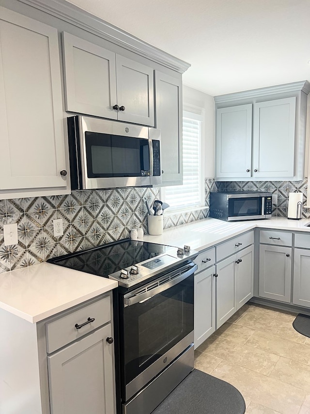 kitchen with gray cabinetry, decorative backsplash, and appliances with stainless steel finishes