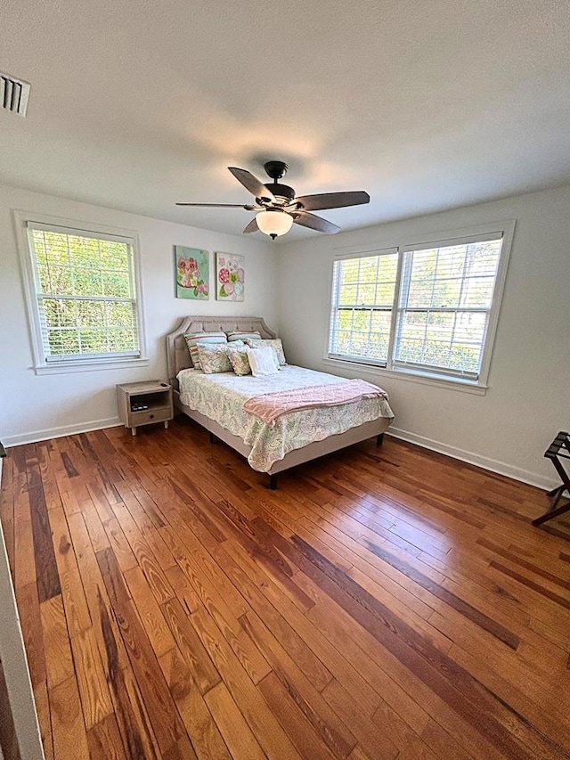 bedroom with multiple windows, dark hardwood / wood-style floors, and ceiling fan