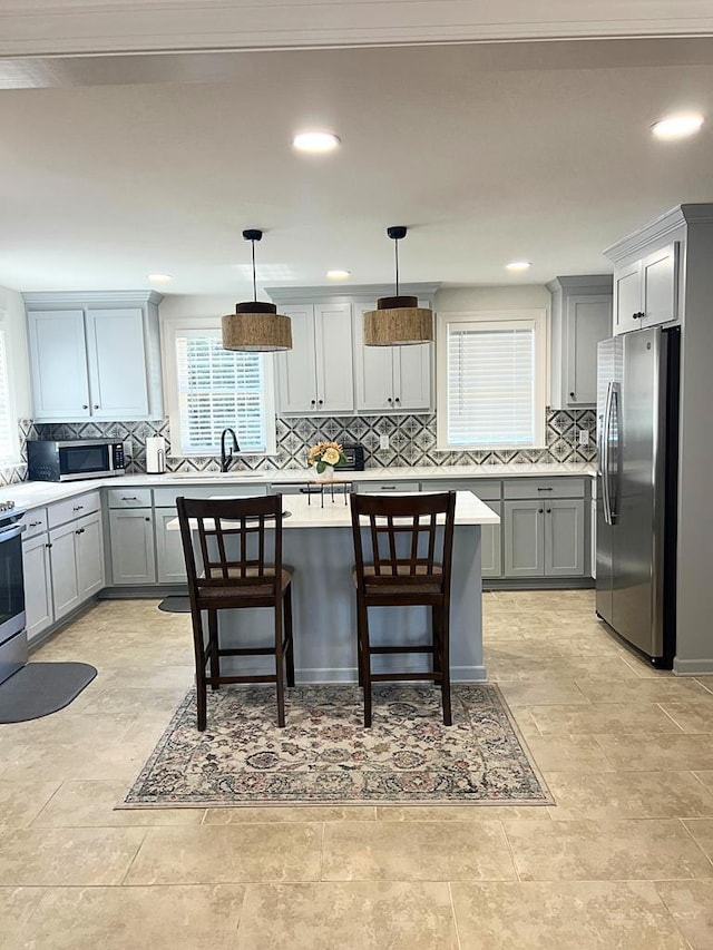 kitchen featuring gray cabinetry, hanging light fixtures, a kitchen breakfast bar, and appliances with stainless steel finishes