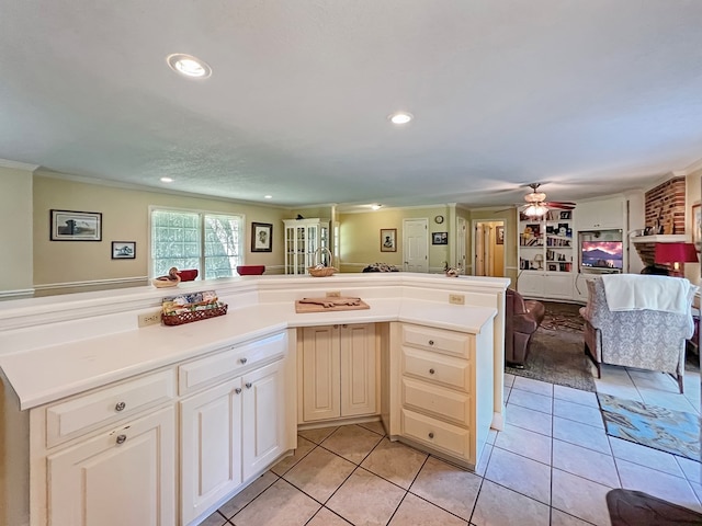 kitchen featuring ceiling fan, a brick fireplace, kitchen peninsula, crown molding, and light tile patterned floors