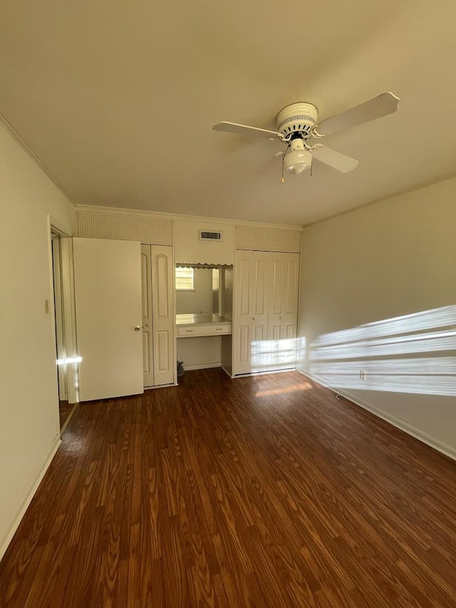 unfurnished living room featuring crown molding, dark hardwood / wood-style flooring, ceiling fan, and built in desk