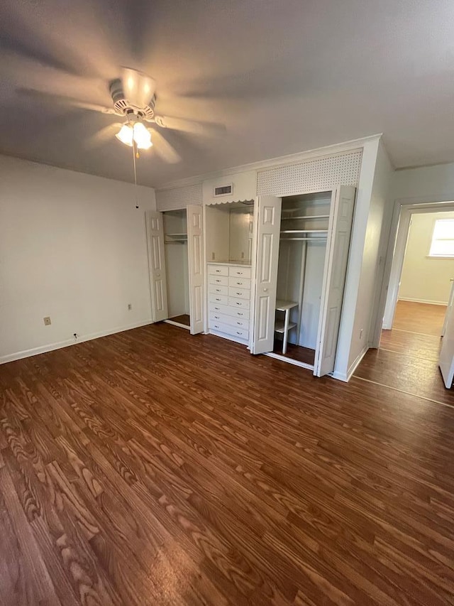 unfurnished bedroom featuring dark hardwood / wood-style flooring, two closets, ceiling fan, and crown molding