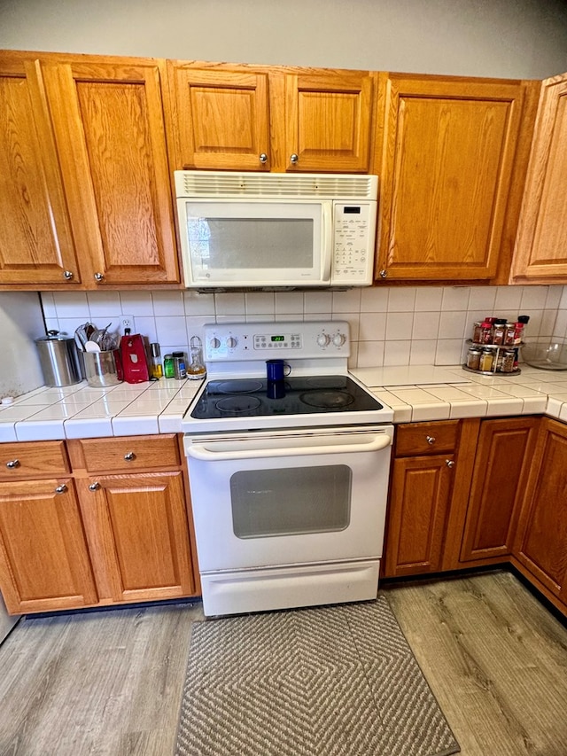 kitchen with light wood-type flooring, white appliances, tile countertops, and tasteful backsplash