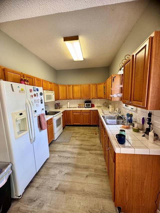 kitchen with sink, light hardwood / wood-style flooring, backsplash, tile countertops, and white appliances