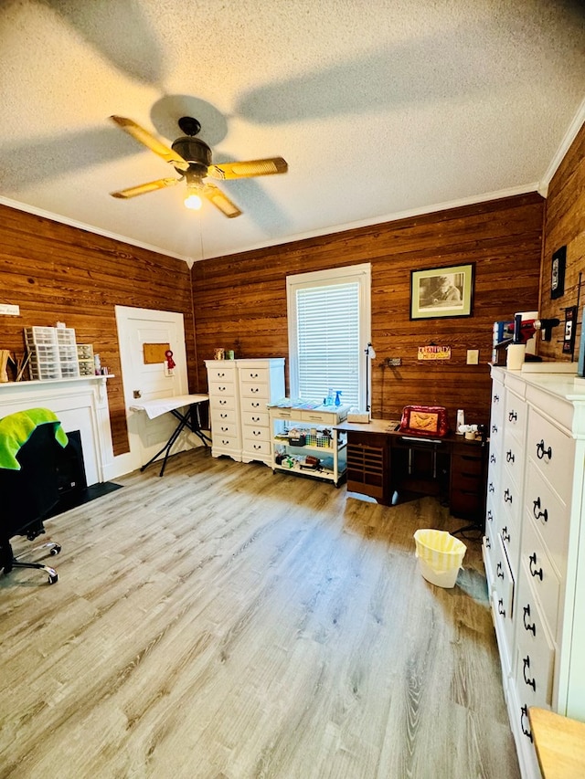 interior space with light wood-type flooring, a textured ceiling, ceiling fan, crown molding, and wooden walls