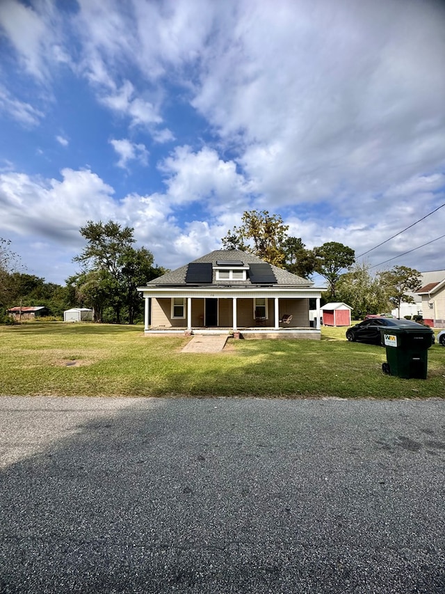 view of front of property with solar panels, covered porch, a front yard, and a storage shed