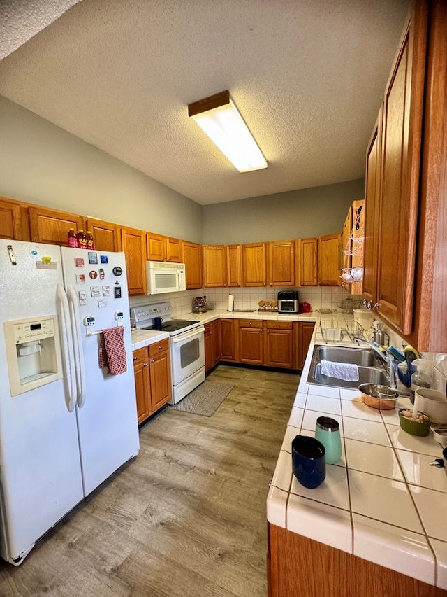 kitchen with decorative backsplash, white appliances, sink, light hardwood / wood-style floors, and tile counters