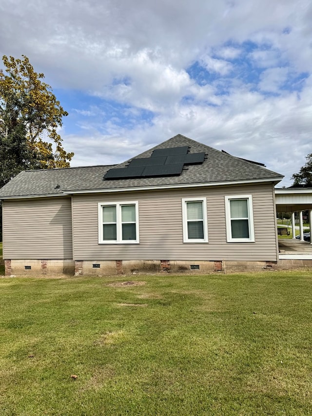 back of property with solar panels and a lawn